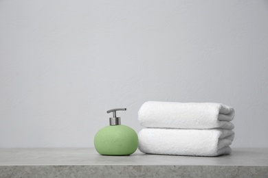 Clean towels and soap dispenser on table against grey background