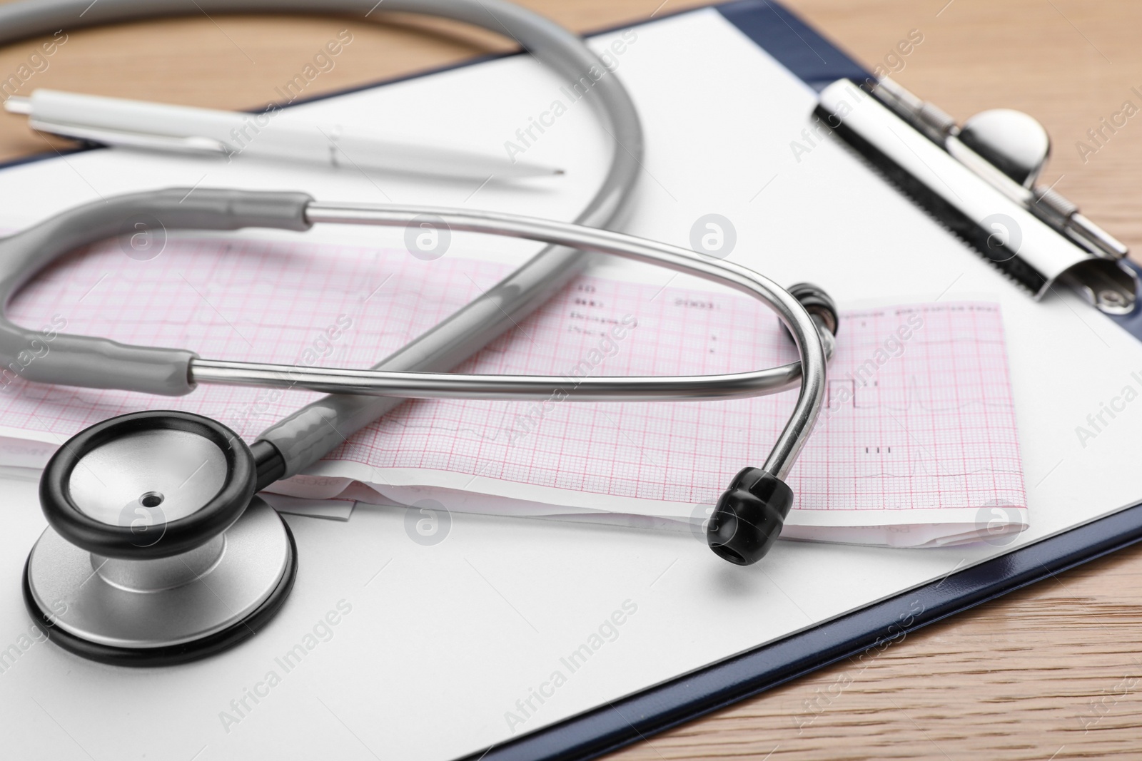 Photo of Clipboard with stethoscope and cardiogram on wooden table, closeup