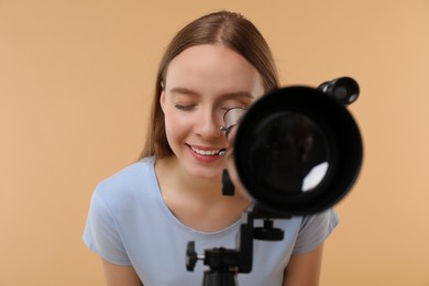 Young astronomer looking through telescope on beige background