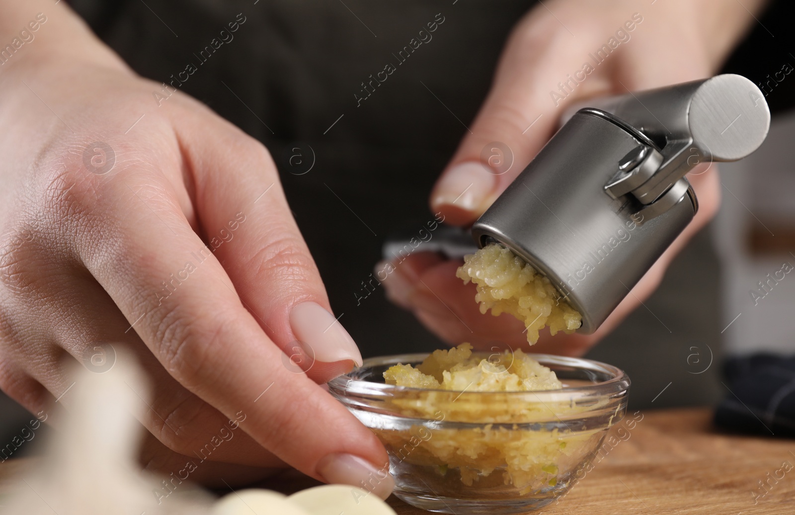 Photo of Woman squeezing garlic with press at wooden table, closeup