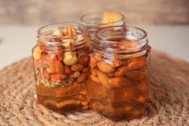 Photo of Jars with different nuts and honey on wicker mat, closeup