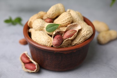 Fresh unpeeled peanuts in bowl on grey table, closeup