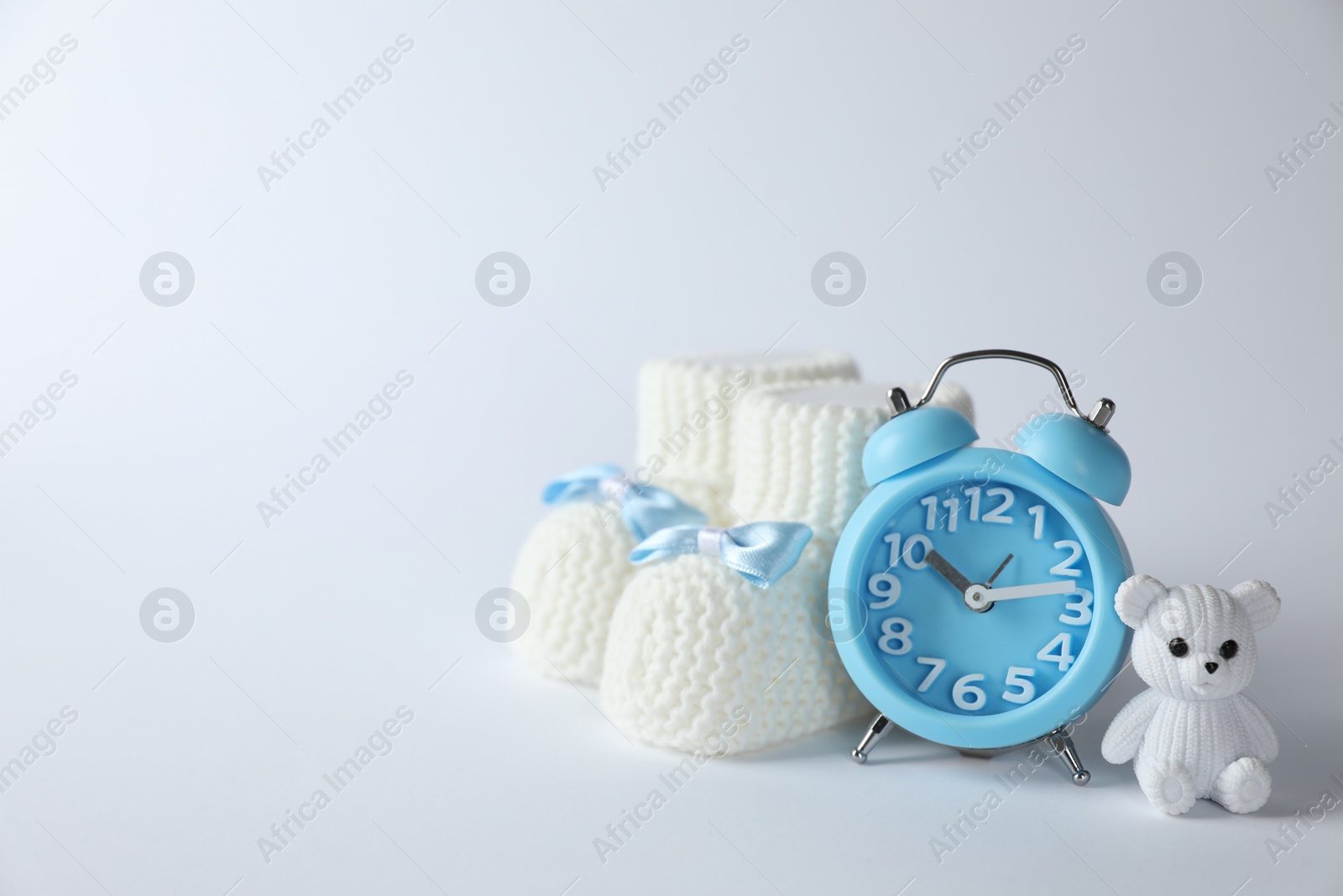 Photo of Alarm clock, toy bear and baby booties on white background, space for text. Time to give birth