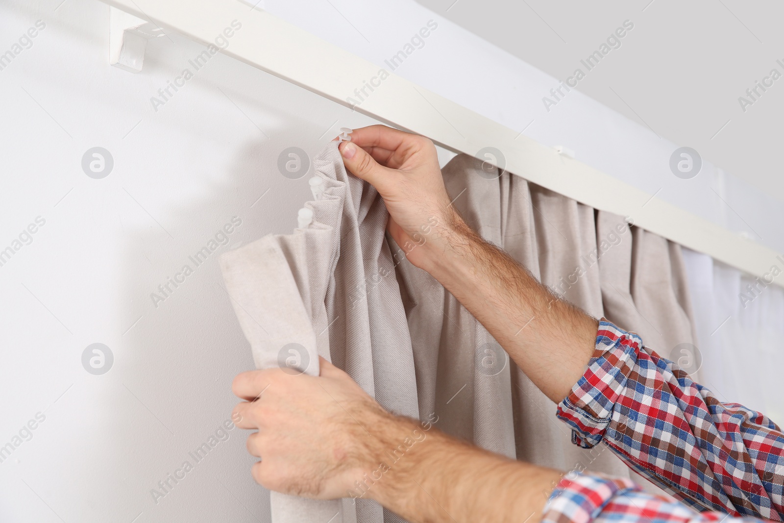 Photo of Man hanging window curtain indoors, closeup. Interior decor element