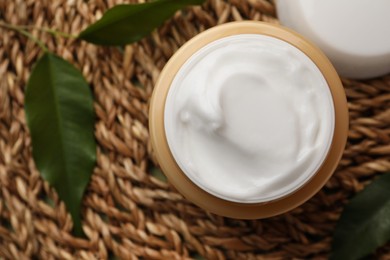 Jar of face cream and fresh leaves on wicker mat, top view. Space for text