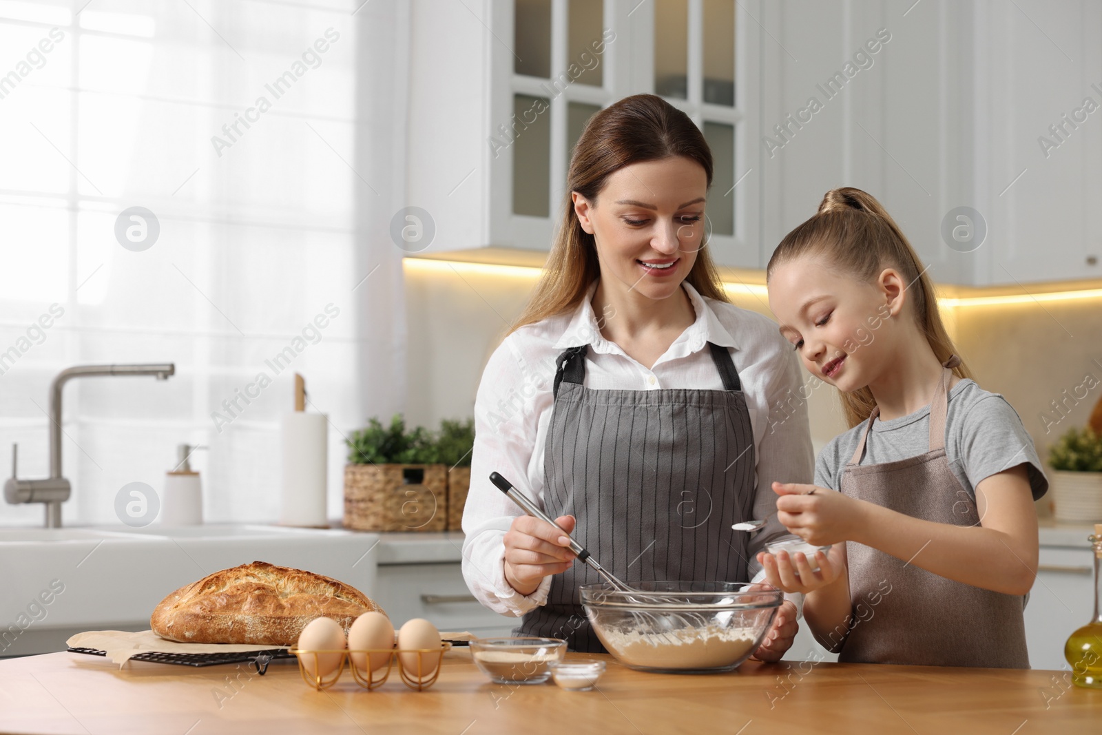 Photo of Making bread. Mother and her daughter preparing dough at wooden table in kitchen