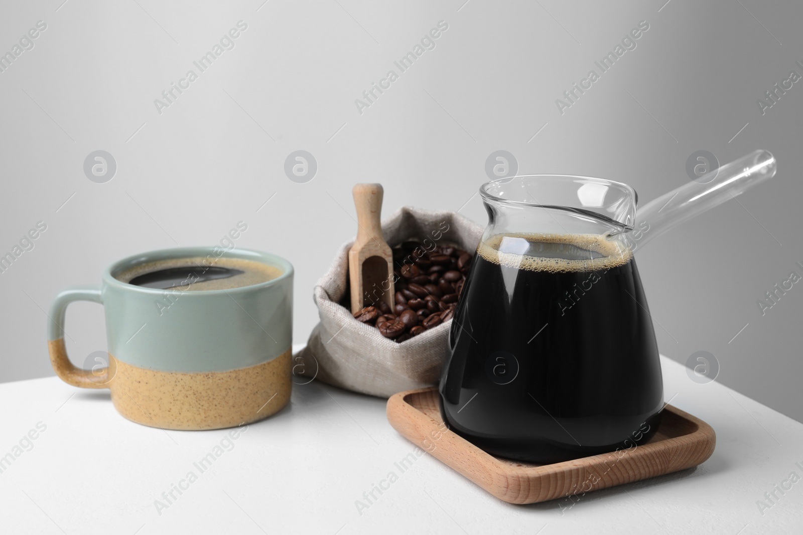 Photo of Turkish coffee. Glass cezve, cup and bag of beans on white table