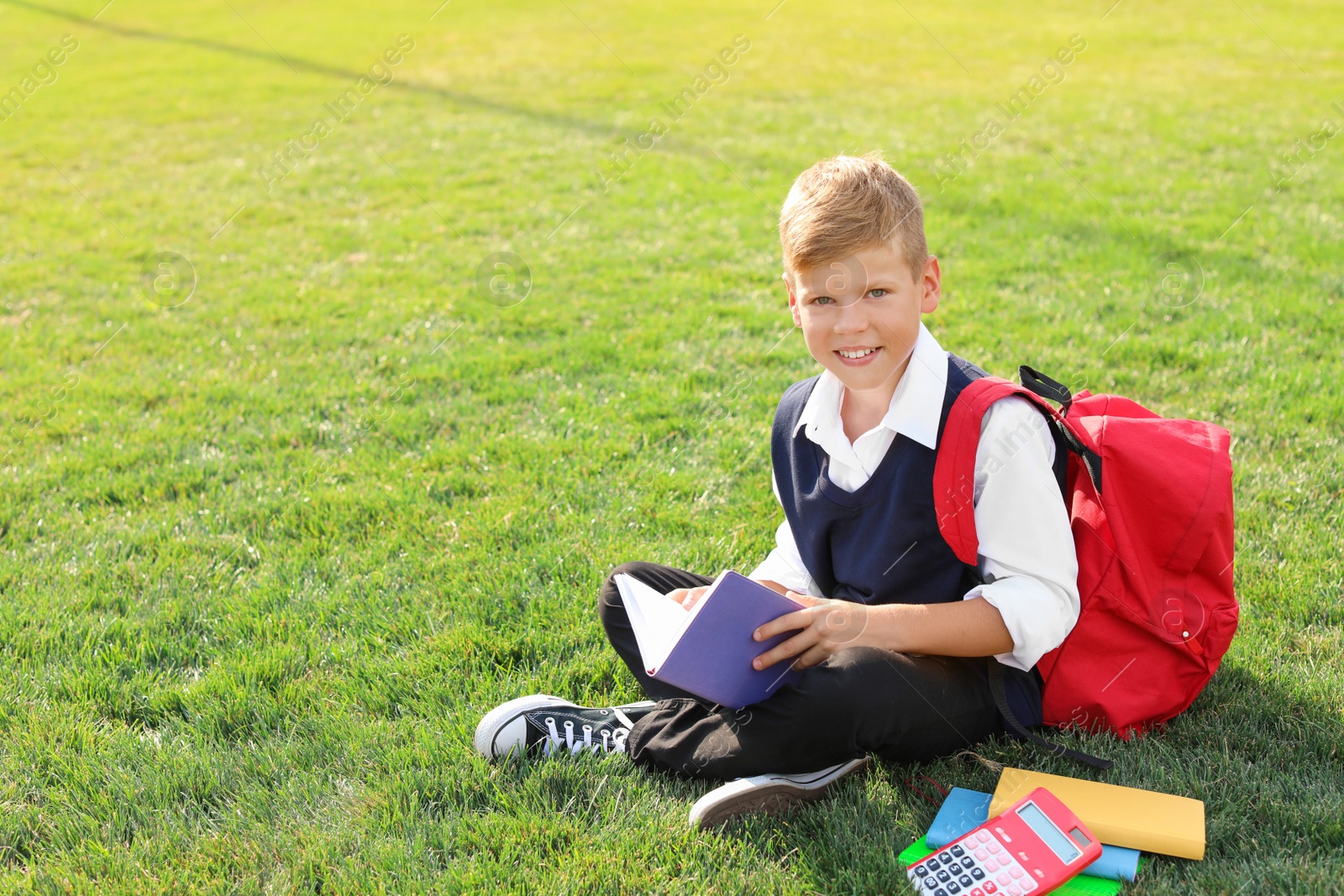 Photo of Schoolboy with stationery sitting on grass outdoors