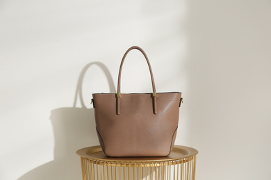 Photo of Stylish leather woman's bag on table near light wall