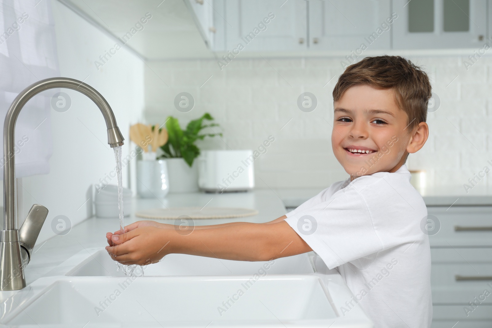 Photo of Boy holding hands under water running from tap in kitchen