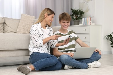Happy mother and her teenage son spending time together with devices on floor at home