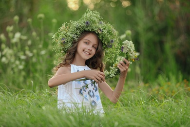 Photo of Cute little girl wearing wreath made of beautiful flowers in field