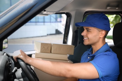 Photo of Young courier with parcels in delivery car