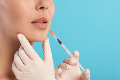 Photo of Doctor giving lips injection to young woman on light blue background, closeup and space for text. Cosmetic surgery