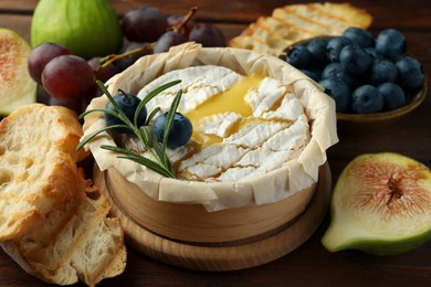 Tasty baked brie cheese and products on wooden table, closeup