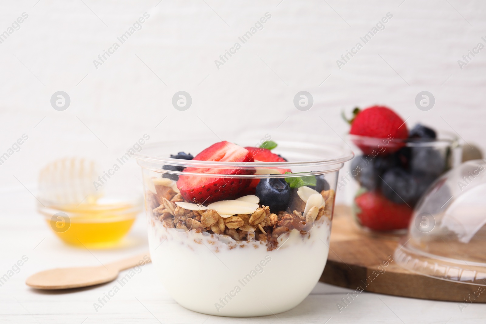 Photo of Tasty granola with berries, yogurt and almond flakes in plastic cup on white table, closeup