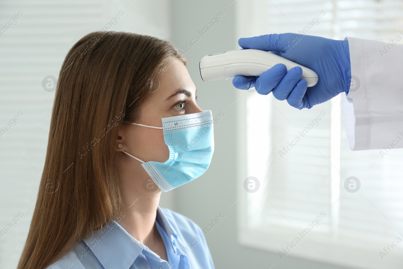 Photo of Doctor measuring patient's temperature with non contact infrared thermometer in office, closeup