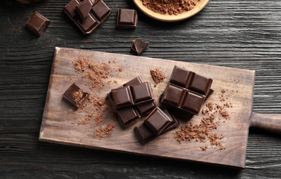 Photo of Pieces of black chocolate on wooden table, top view