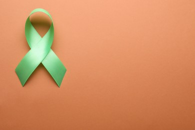 Photo of World Mental Health Day. Green ribbon on pale orange background, top view with space for text