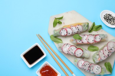 Delicious spring rolls served on light blue background, flat lay