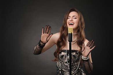 Photo of Beautiful young woman in stylish dress with microphone singing on dark background