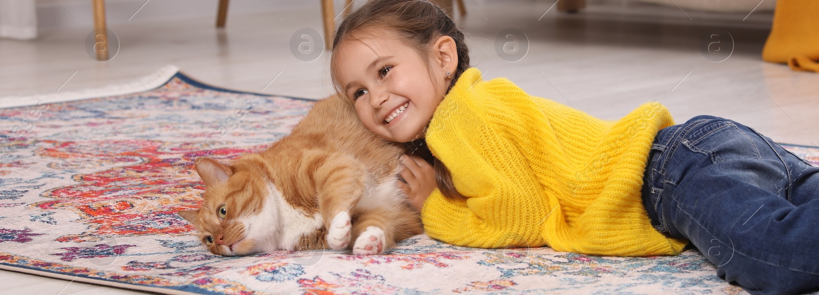 Image of Happy little girl and cute ginger cat on carpet at home. Banner design