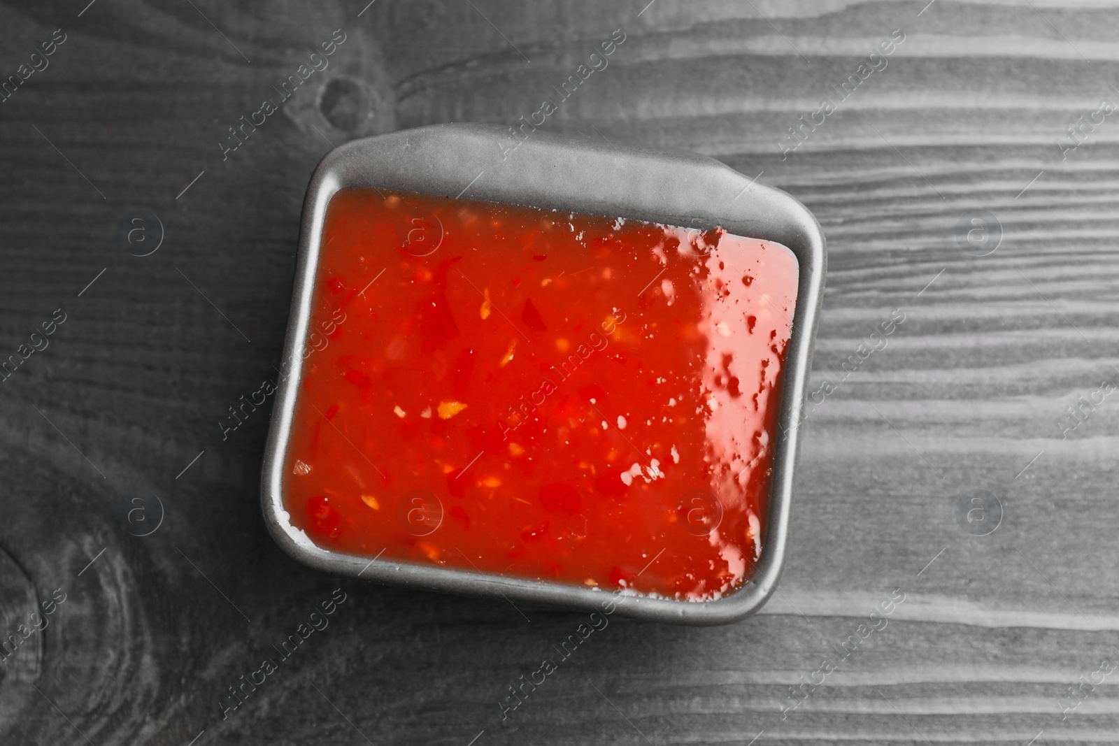 Photo of Spicy chili sauce in bowl on black wooden table, top view