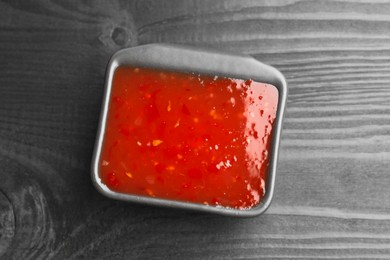 Photo of Spicy chili sauce in bowl on black wooden table, top view