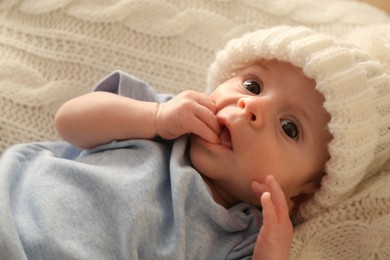 Cute little baby wearing white warm hat on knitted blanket, closeup