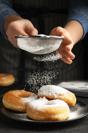 Photo of Woman decorating delicious donuts with powdered sugar at black table, closeup