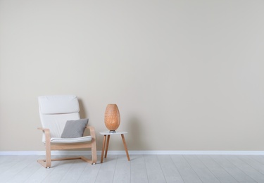 Comfortable armchair and lamp on table near color wall with space for text. Interior element