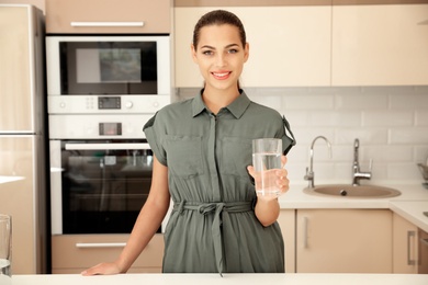 Photo of Young woman holding glass with water in kitchen