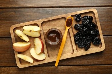 Tasty baby food in jar, cut apple and dried prunes on wooden table, top view