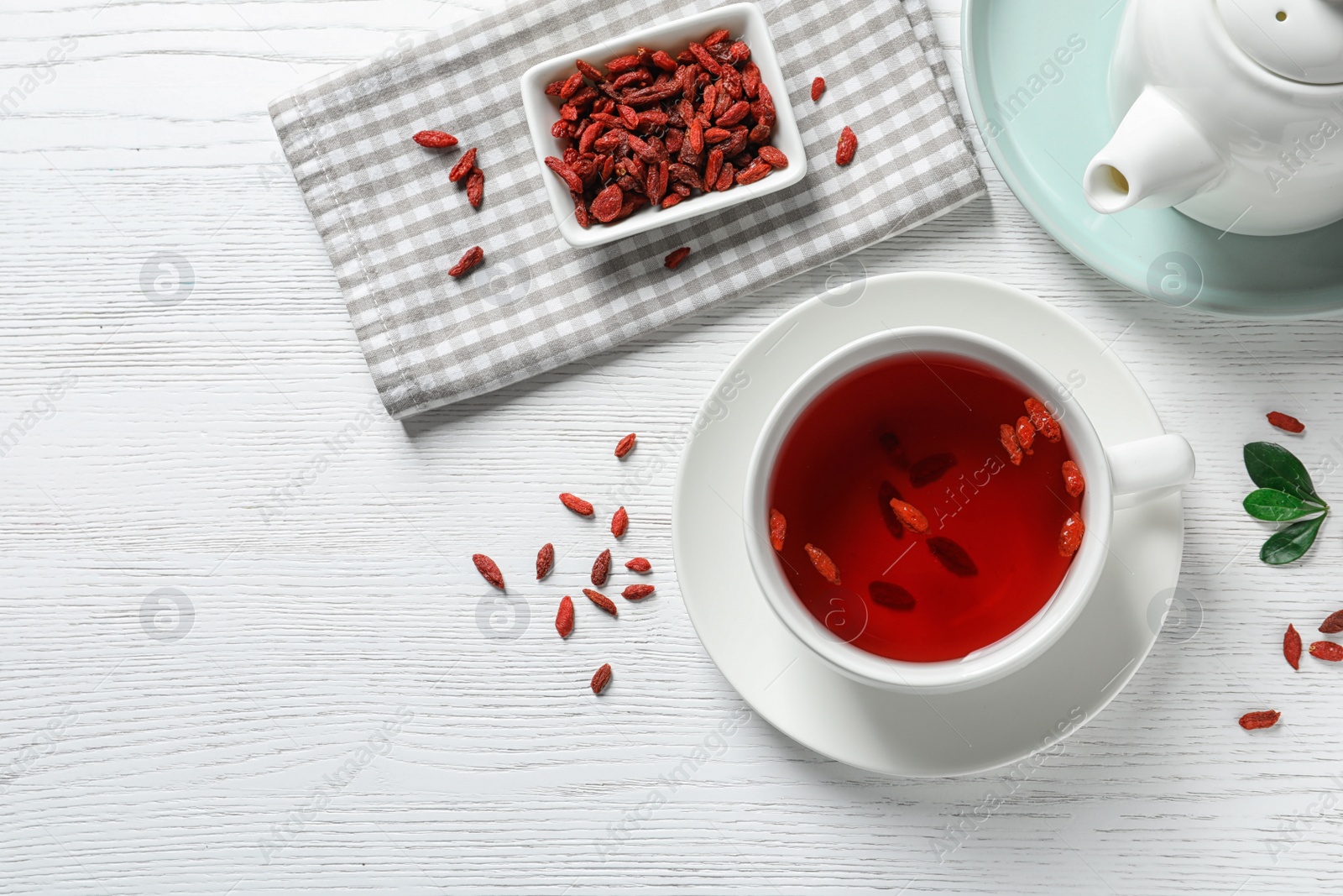 Photo of Healthy goji tea in cup served on white wooden table, flat lay. Space for text