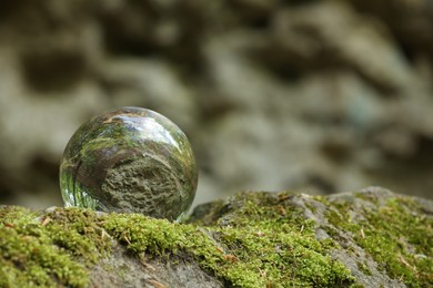 Photo of Beautiful forest, overturned reflection. Crystal ball on stone surface with moss outdoors. Space for text