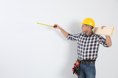 Photo of Handsome carpenter with wooden planks and measuring tape on light background. Space for text