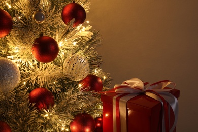 Beautiful decorated Christmas tree with glowing fairy lights and present on beige background