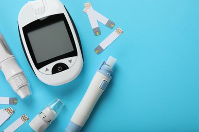 Photo of Digital glucometer, lancet pens and test strips on light blue background, flat lay with space for text. Diabetes control