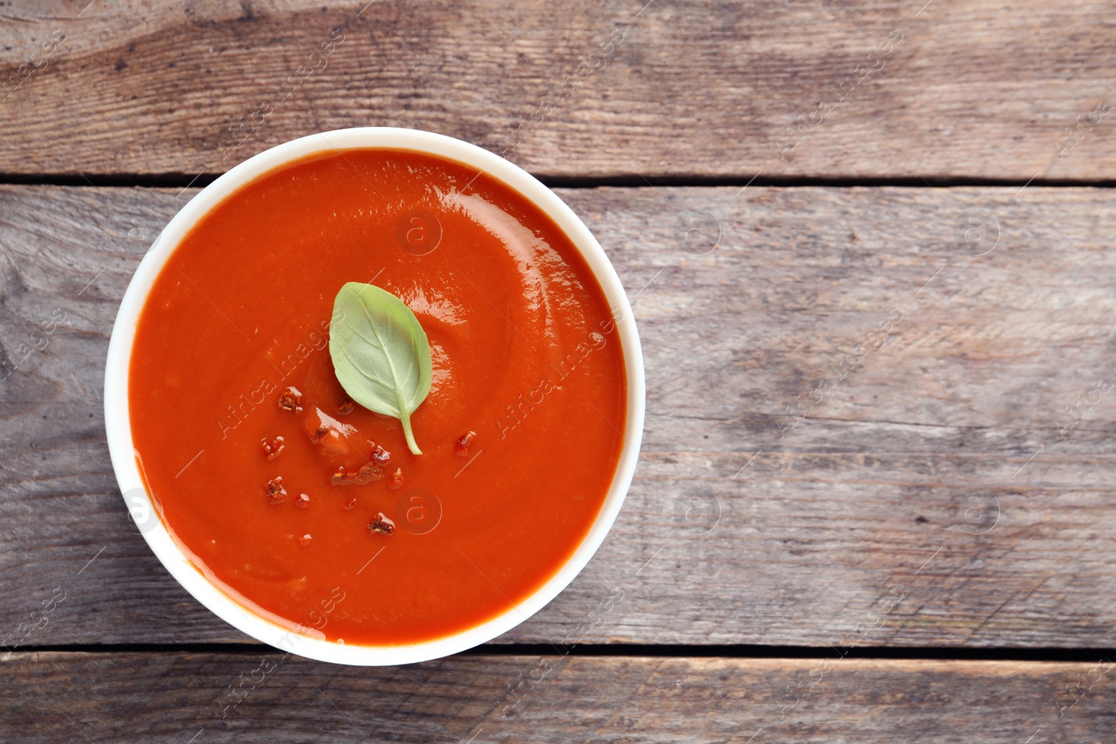 Photo of Bowl with fresh homemade tomato soup and space for text on wooden background, top view