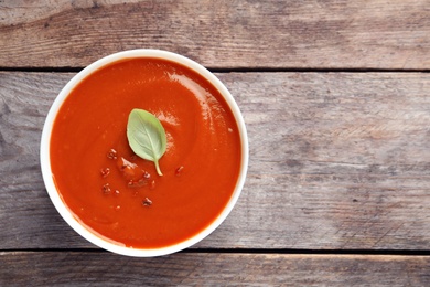 Photo of Bowl with fresh homemade tomato soup and space for text on wooden background, top view