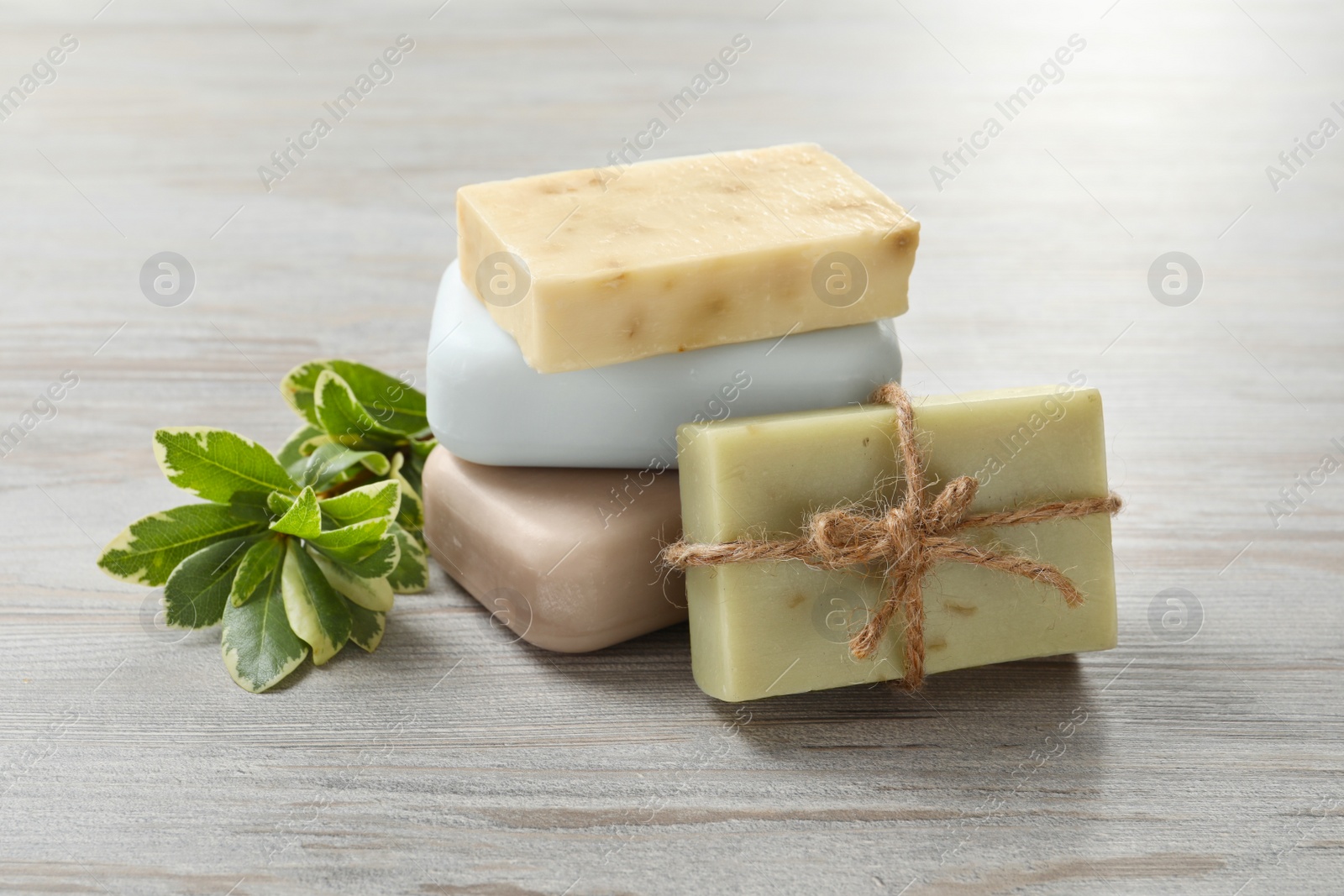 Photo of Stack of different soap bars and green plant on white wooden table, closeup