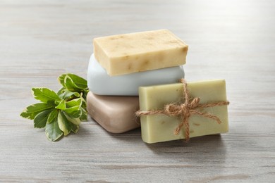 Photo of Stack of different soap bars and green plant on white wooden table, closeup