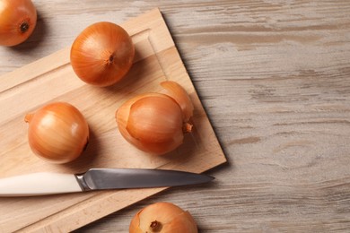 Photo of Many ripe onions and knife on wooden table, flat lay. Space for text