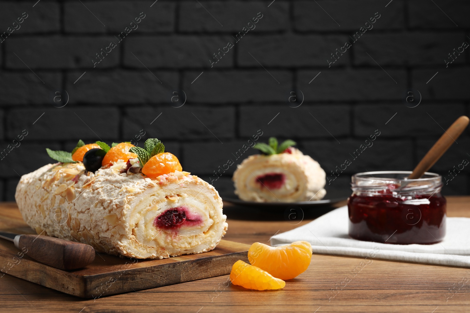 Photo of Tasty meringue roll with jam, tangerine slices and mint leaves on wooden table. Space for text