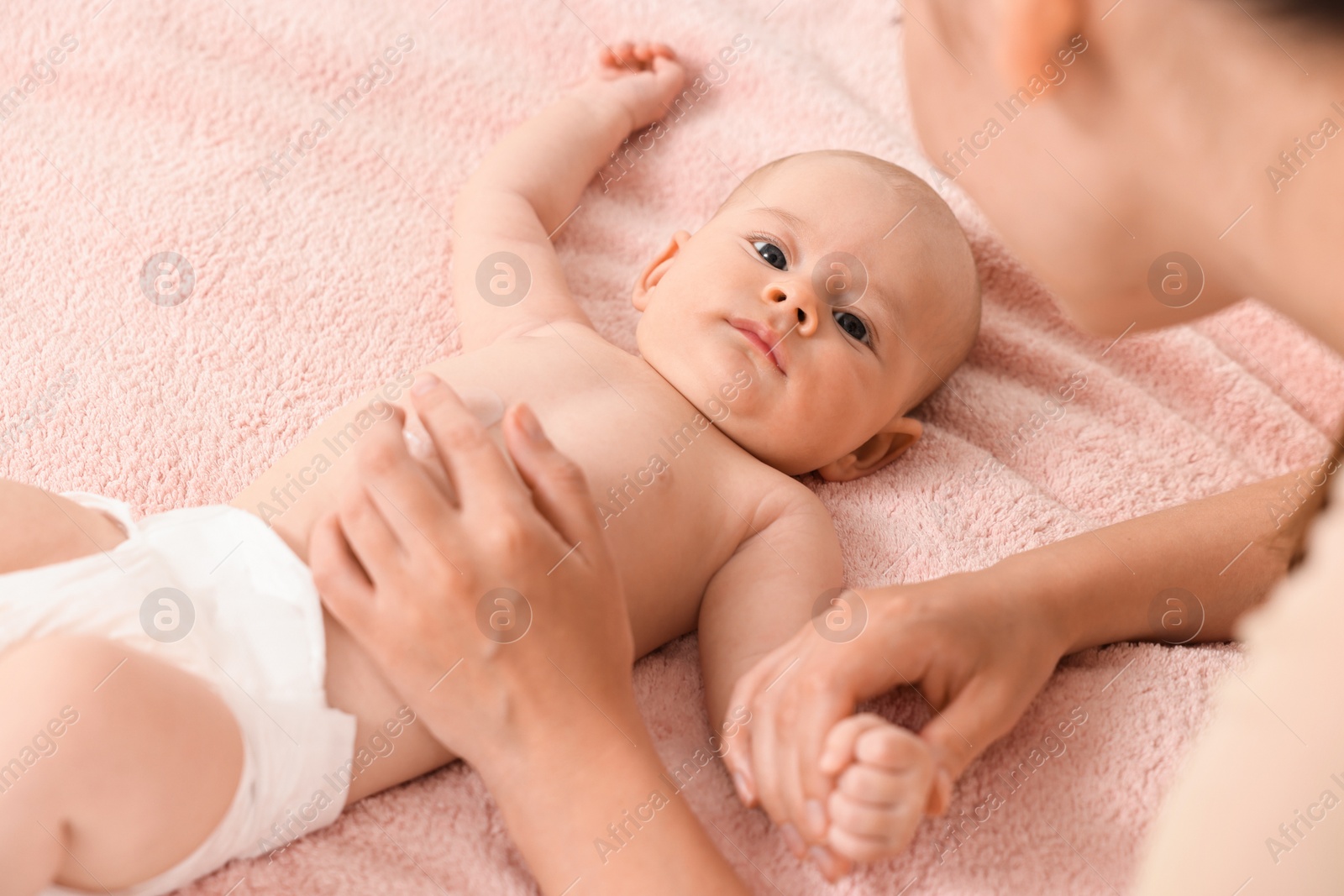 Photo of Woman applying body cream onto baby`s skin on bed, closeup