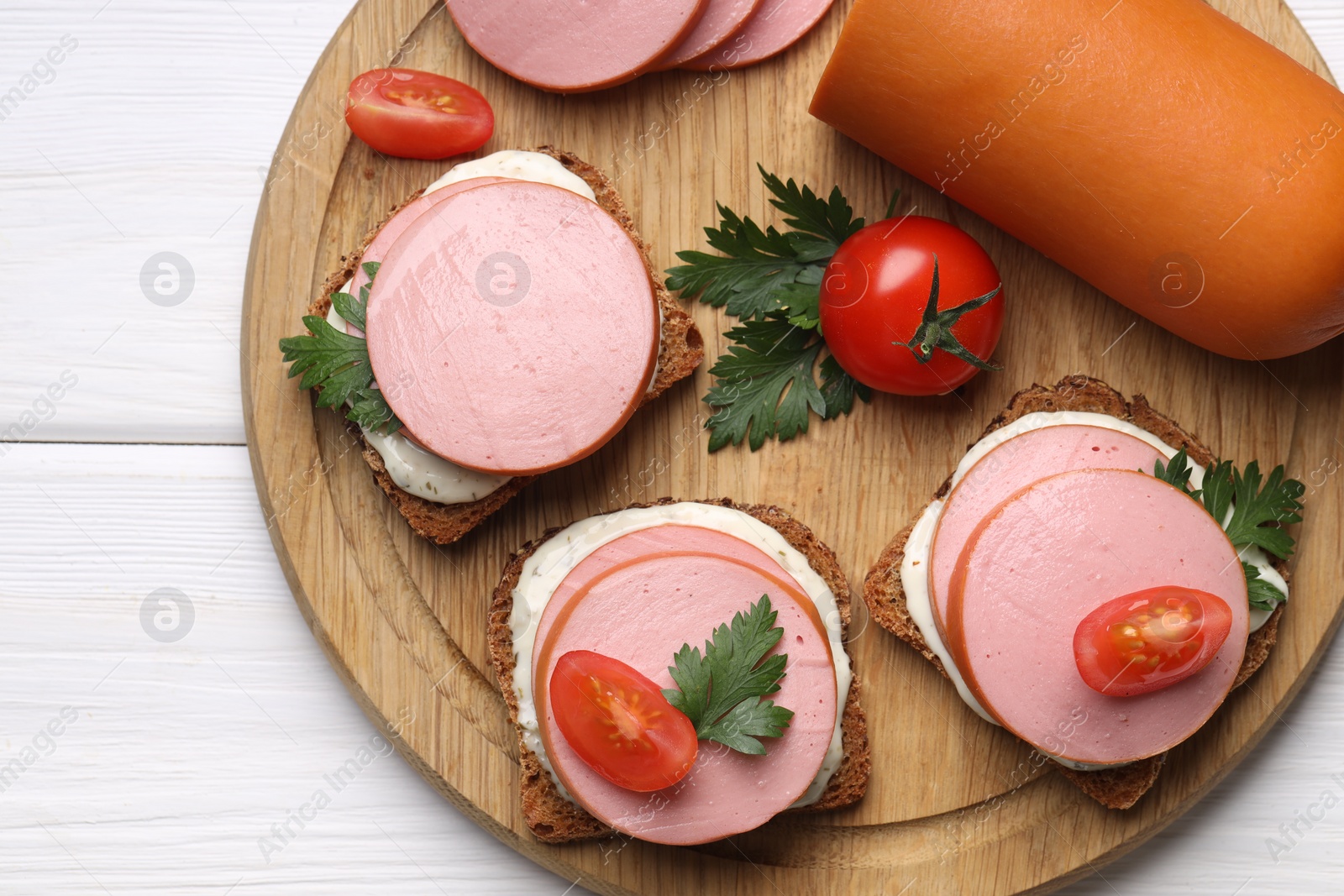 Photo of Delicious sandwiches with boiled sausage, tomato and sauce on white wooden table, top view