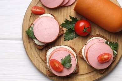 Photo of Delicious sandwiches with boiled sausage, tomato and sauce on white wooden table, top view