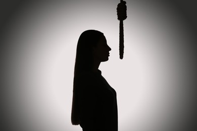 Photo of Silhouette of woman with rope noose on light background