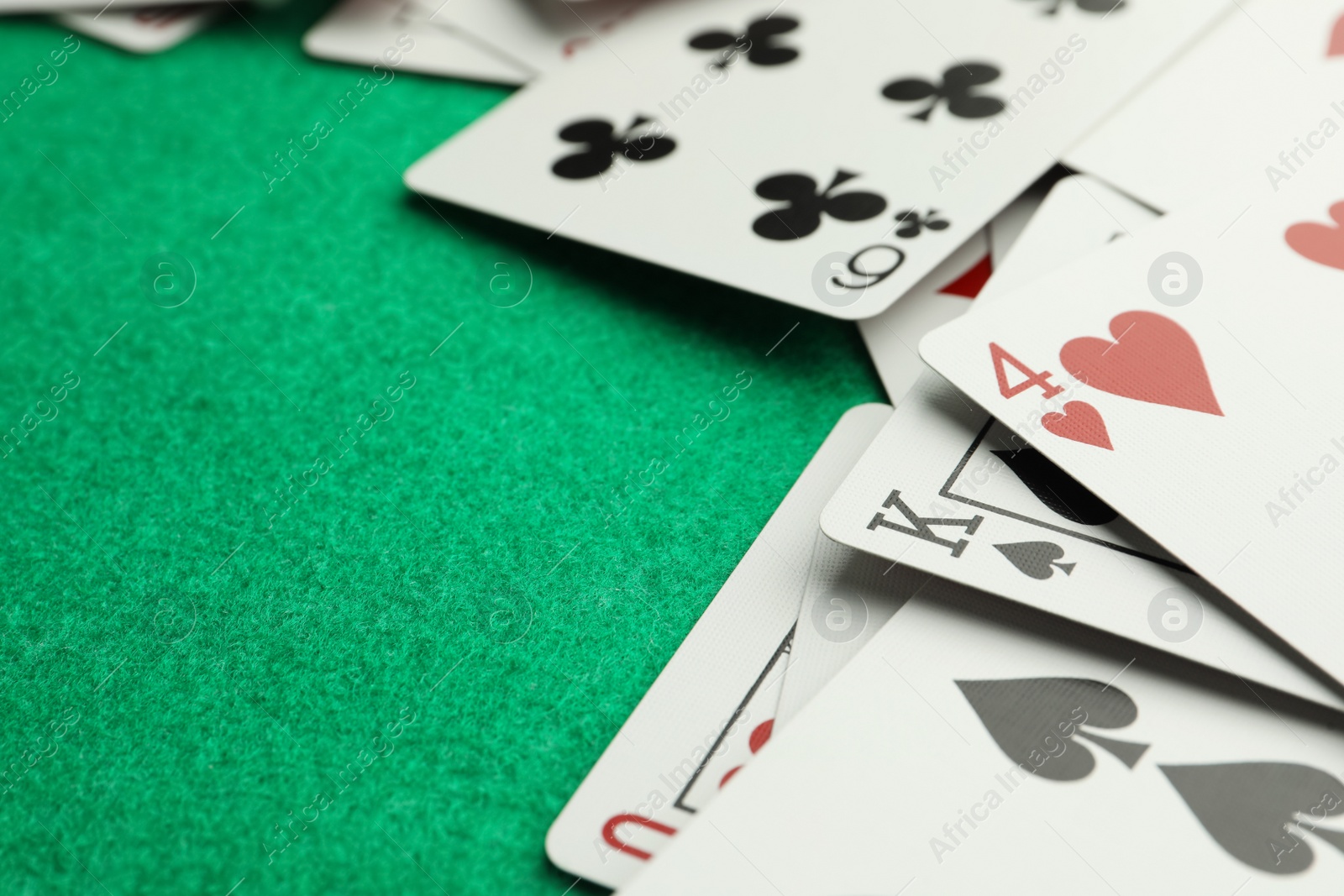Photo of Scattered playing cards on green table, closeup. Space for text