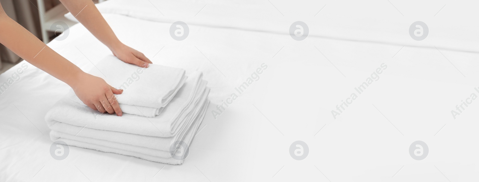 Image of Woman putting clean white towels on bed, closeup with space for text. Banner design